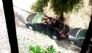Un homme protège sa voiture lors d'une averse de grêle