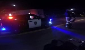 Un motard s'amuse à faire du stunt devant une voiture de police