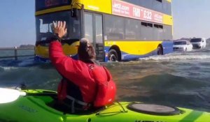 Il fait du kayak sur une route inondée à côté des automobilistes